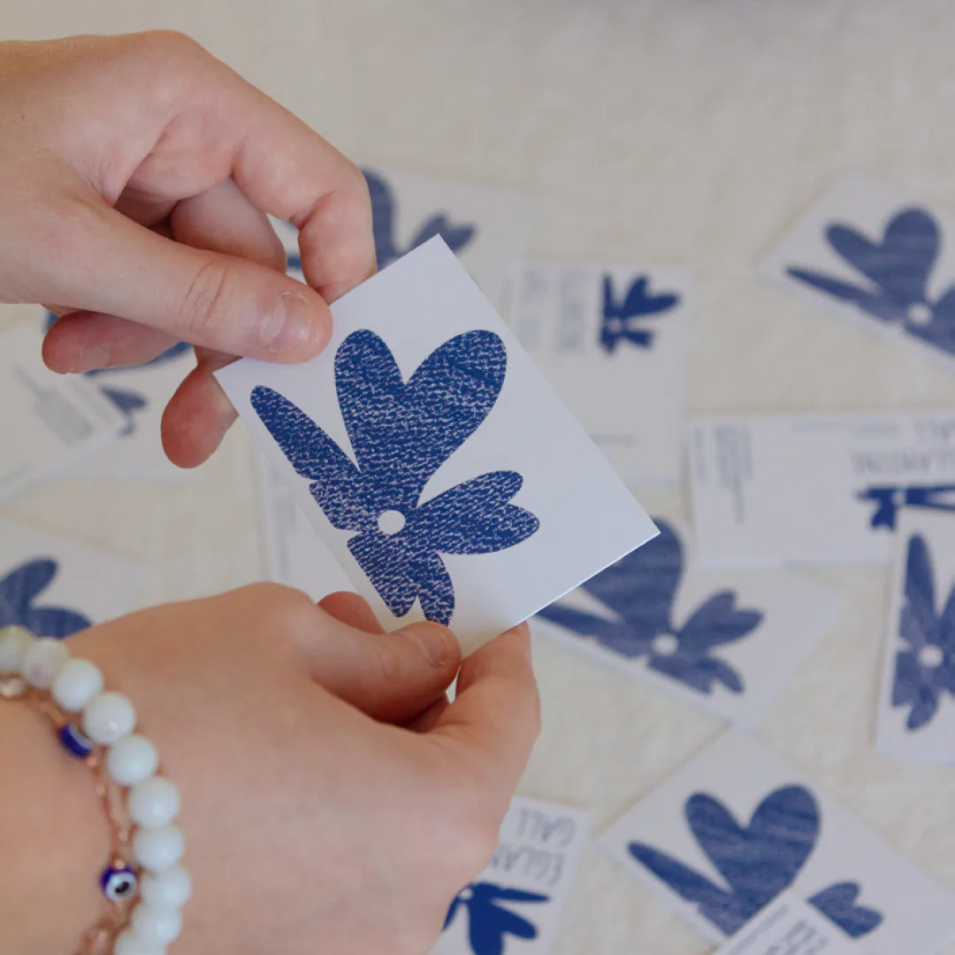 Deux mains tiennent le verso d’une carte de visite d’Églantine Gall, une grande fleur bleue texturée, au-dessus d’autres cartes