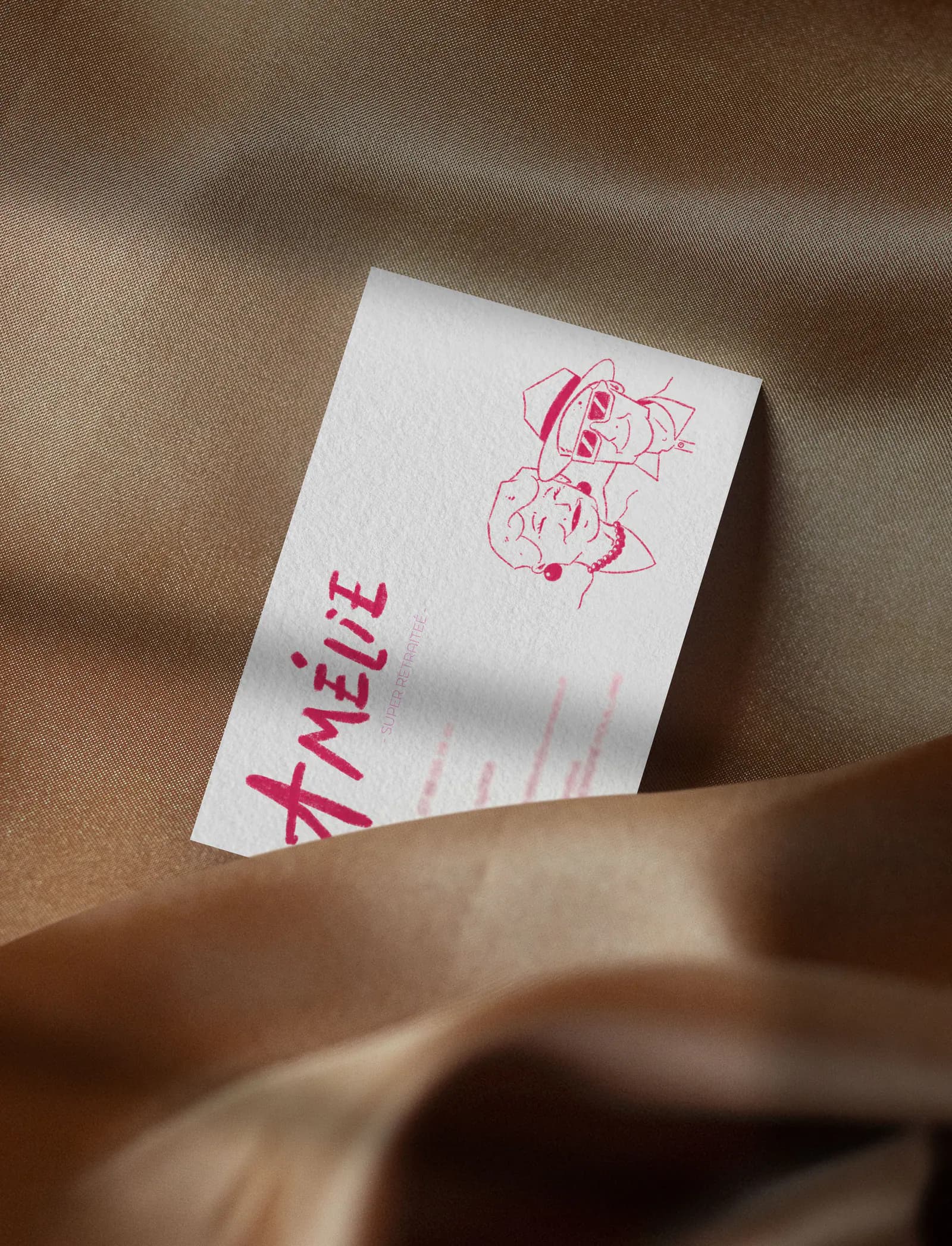 Verso de la carte d’Amélie glissé dans un tissu satiné brun : prénom écrit à la main en rose, portrait du duo en rose, coordonnées floutées