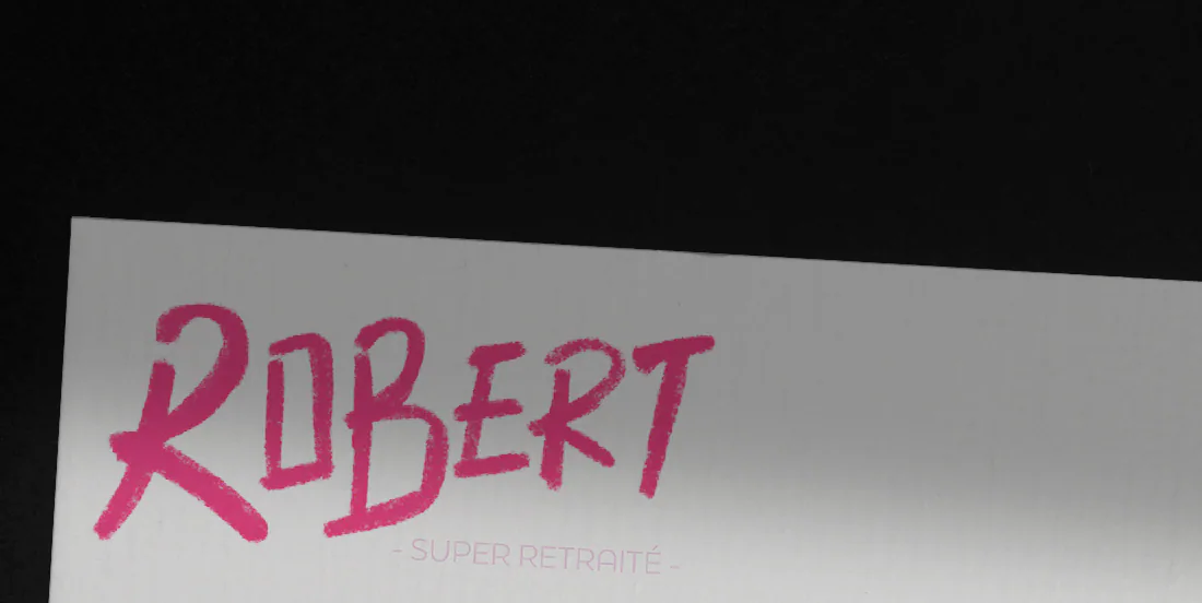 Détail du verso de Robert sur fond noir : son prénom écrit à la main en rose vif et la mention super retraité en petites capitales roses